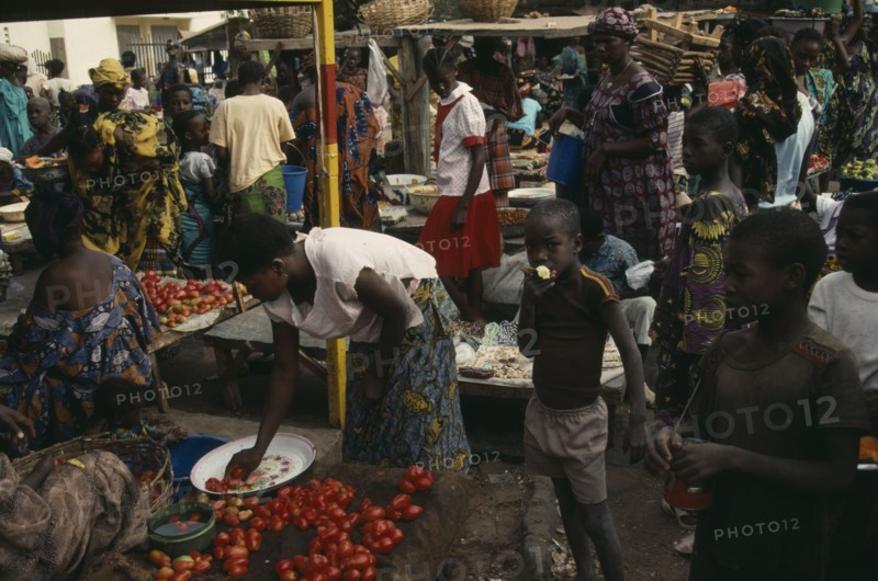 MALI, Kayes, Busy market scene with brightly dressed women and children amongst food stalls.