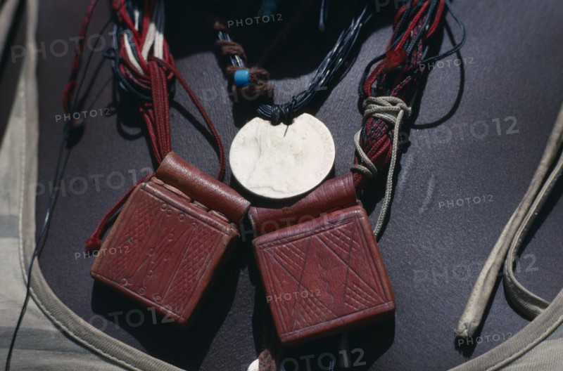 SUDAN, Mornei Settlement, Close view of leather pouches containing verses of the Koran worn as a charm around the neck by Chadian refugee woman together with old French coin and beads.