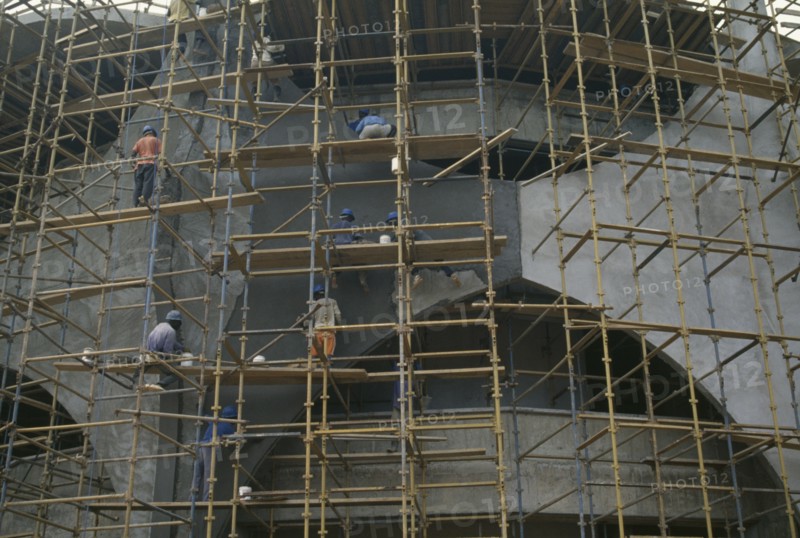 GHANA, Accra, Construction workers on scaffolding surrounding new bank building.