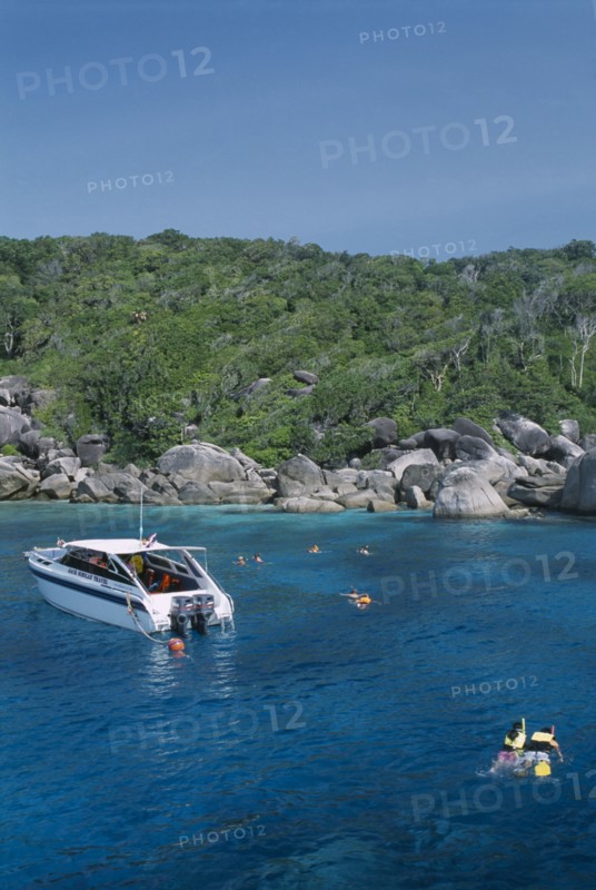 THAILAND, Similan Islands, Ko Bangu, Snorkelers in the water next to a small motor boat near the rocky shore.
