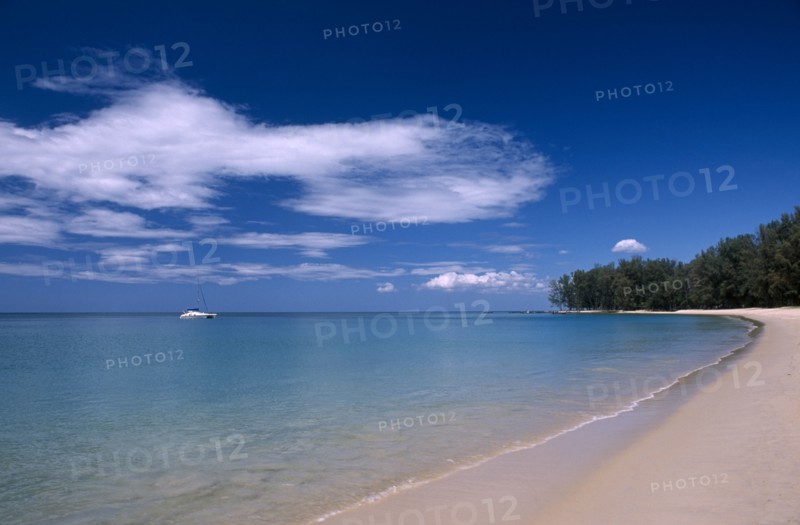 THAILAND, North Phuket, Naiyang Beach, View along the empty sandy beach with a single boat in the blue sea.