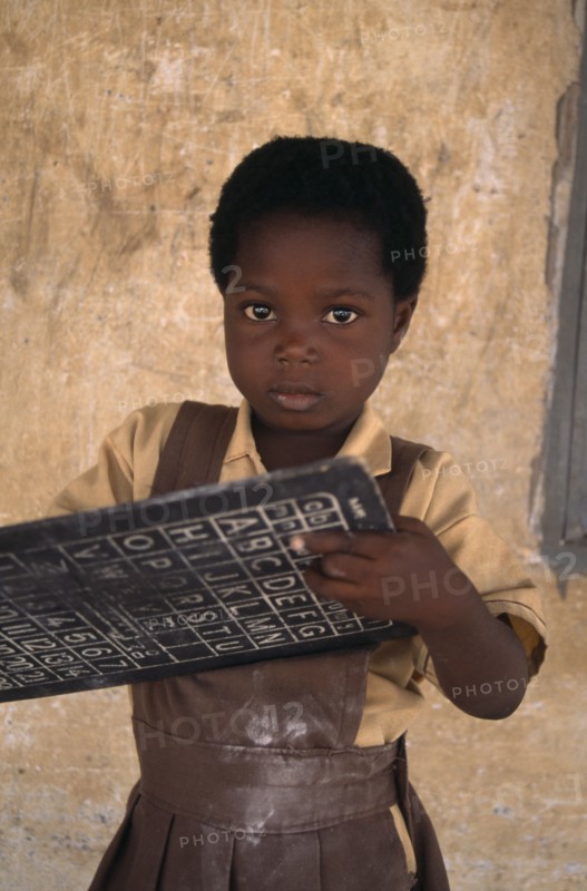 GHANA, Education, Portrait of pupil from primary school in village near Accra holding small blackboard printed with alphabet and numbers.
