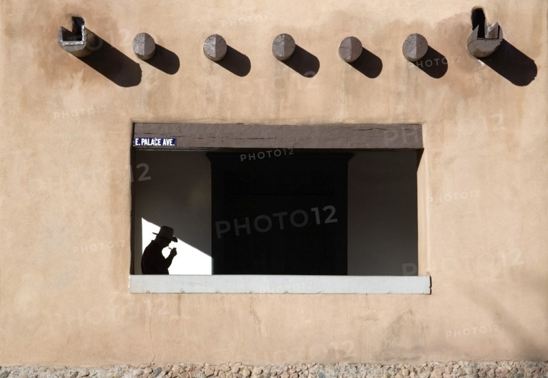 USA, New Mexico, Santa Fe, Detail of the Palace of The Governors in the Plaza with a man wearing a cowboy hat walking under the pueblo style arches