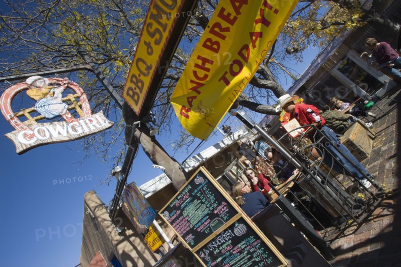 USA, New Mexico, Santa Fe, The Cowgirl Cafe outdoor eating area with customers and a waiter. Sign showing the days meals