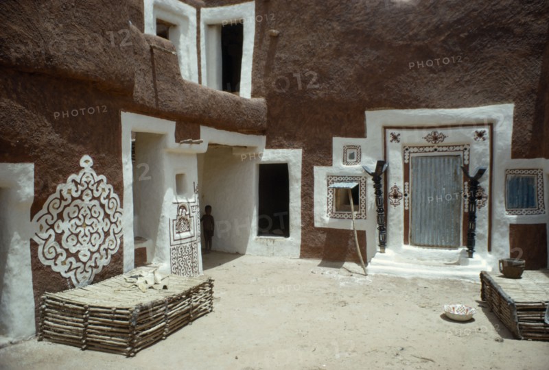 MAURITANIA, Oualata, "Traditional mud architecture decorated with bas relief motifs of applied gypsum, white and red clay.  Small child standing in shadow of corner of building. "