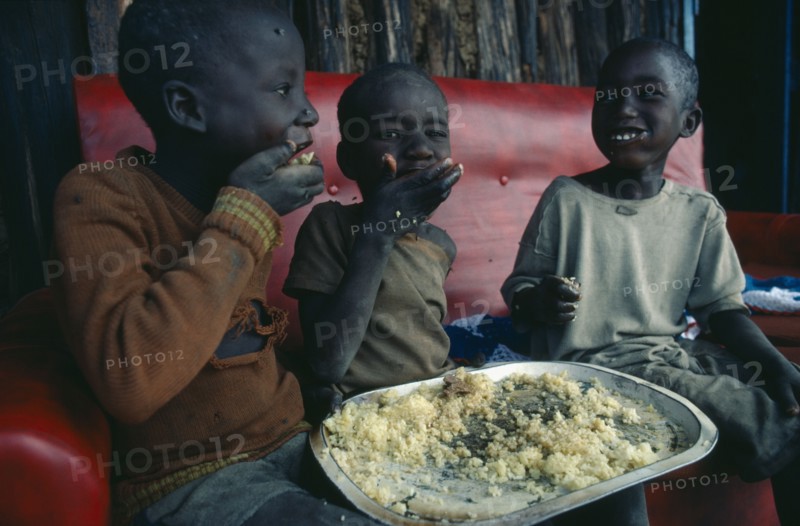 KENYA, Children, Three young children using right hands to eat Christmas lunch.