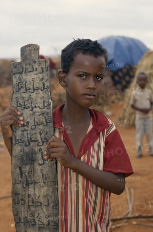 KENYA, Mandera, Somali refugee camp run by UNHCR.  Young boy attending Koranic school holding piece of wood inscribed with Koranic script.
