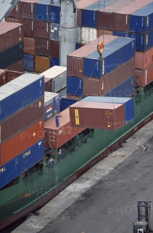 IVORY COAST, San Pédro, Containers being unloaded from vessel docked at San Pédro port.  Worker standing on container to direct crane.
