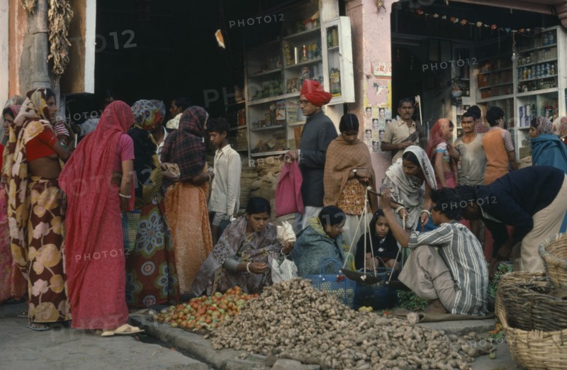 INDIA, Rajasthan, Jaipur, Busy market scene with stall selling tomatoes and ginger laid out on pavement in the foreground and open fronted shops behind.