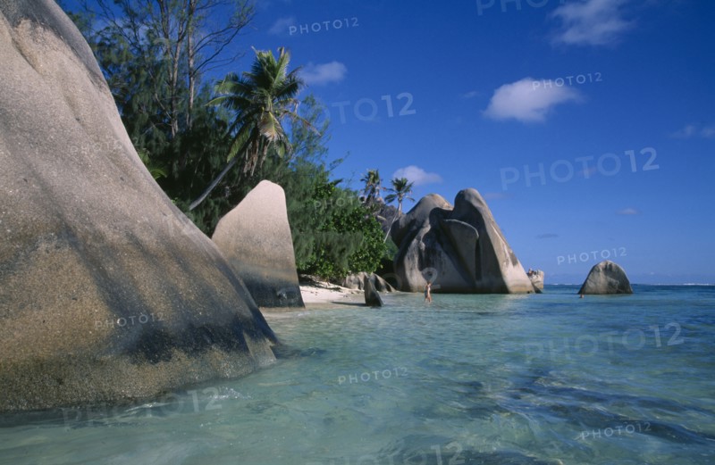 SEYCHELLES, La Digue , Anse Source D Argent, Rock formations along the coast with a woman bather walking into the turquoise sea