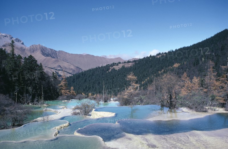 CHINA, Sichuan Province, Huanglong, View across pools formed by calcium carbonate in water towards green forest and mountains