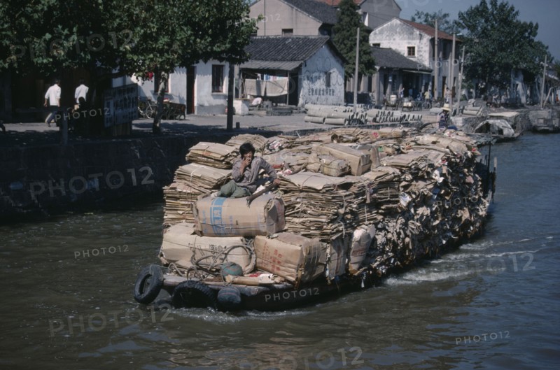 CHINA, Jiangsu Province, Suzhou, Man on boat travelling along the Grand Canal carrying piles of cardboard between Suzhou to wuxi