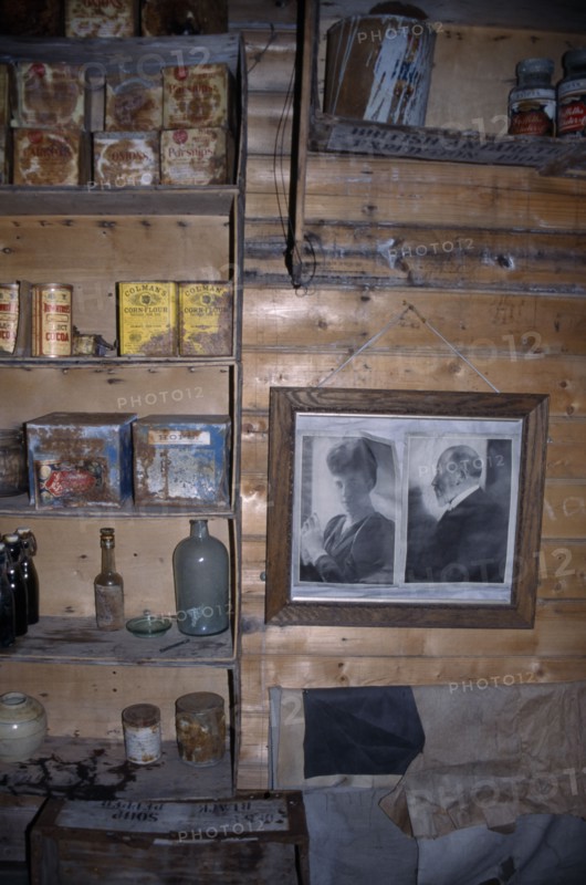ANTARCTICA, Ross Sea, Ross Island, Cape Royds. Interior of Shackletons Hut built in 1908 with framed photographs on the wall and shelves with rusty tinned food containers