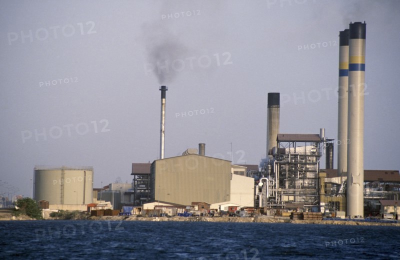 CURACAO, Willemstad, Seawater desalination plant exterior with narrow chimney emitting black smoke.