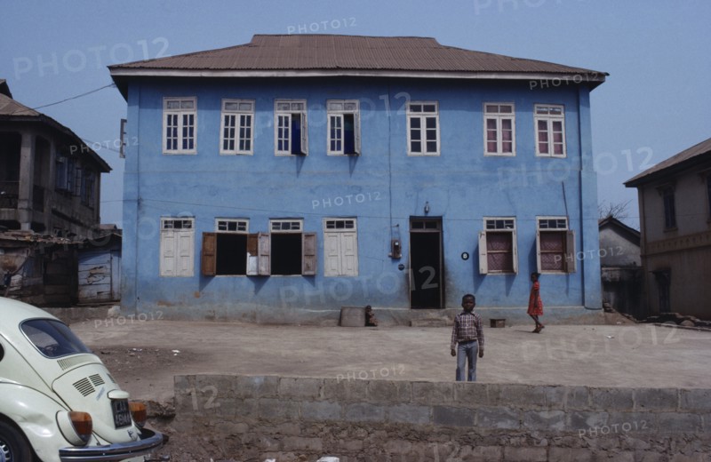 NIGERIA, Inagbiji, Blue painted exterior of typical house with wooden shutters and children in yard outside.