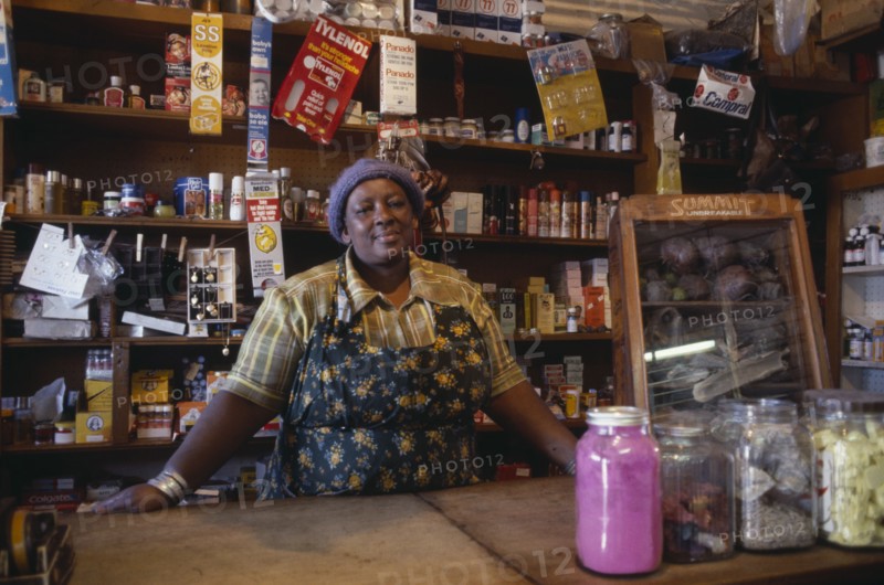 SOUTH AFRICA, Gauteng, Soweto, Portrait of shopkeeper behind counter with goods arranged on shelves behind her.