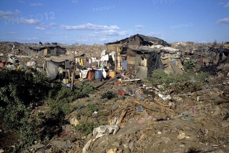 NICARAGUA, Managua Province, Managua, "The 'waste basket of Chureca' has existed since the late 1960's in the Acahualinca district of Managua, Nicaragua. It covers 42 hectares, is bombarded with thousands of tonnes of waste a day and is home to over 170 struggling families. By day over 1500 more Nicaraguans arrive at the site, some of whom are children who have been sent by their parents, others come by their own initiative. All compete with the adults to find, harvest and re-sell recyclable material. Of the minors who go to the waste basket - 88% it has respiratory problems, 62% suffer from parasites and 42% have serious skin diseases. Although the sky is clear and blue the air is thick of burning waste or rotting waste. Little houses or 'casitas' lie in a mixed muddle of rubbish and waste. The house at the front of shot is made up of an eclectic collection of doors, wooden planks, dustbin bags, hanging bits of ripped tarpaulin, corrugated iron strips and whatever waste material seems...