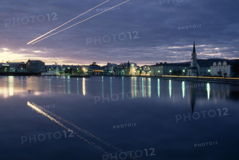 ICELAND, Reykjavik, The Tjörn or lake in city centre at night with light from street lamps reflected across flat surface.