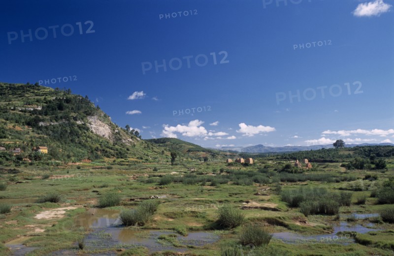 MADAGASCAR, Landscape, Road to Ambalavao. View across green flood plain  towards clay brick kilns and tree covered hills