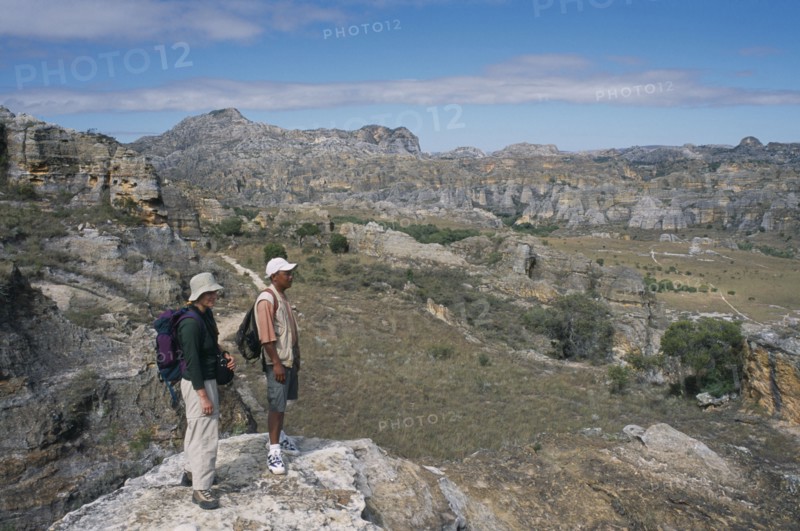 MADAGASCAR, Isalo National Park, Tourist and guide standing on edge of rock looking over craggy sandstone massifs