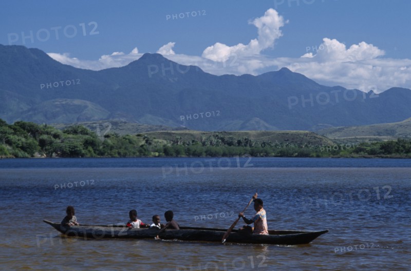 MADAGASCAR, Fort Dauphin, Lokaro, Mother ferrying her children across the bay in a Pirogue with mountains in the distance