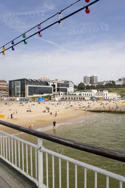 ENGLAND, Dorset, Bournemouth, The East Beach from the pier with seafront restaurants and bars. Adults and children play in the sand on the beach and at the water's edge between the groynes. Hotels and flats line the clifftop into the distance Paul Seheult