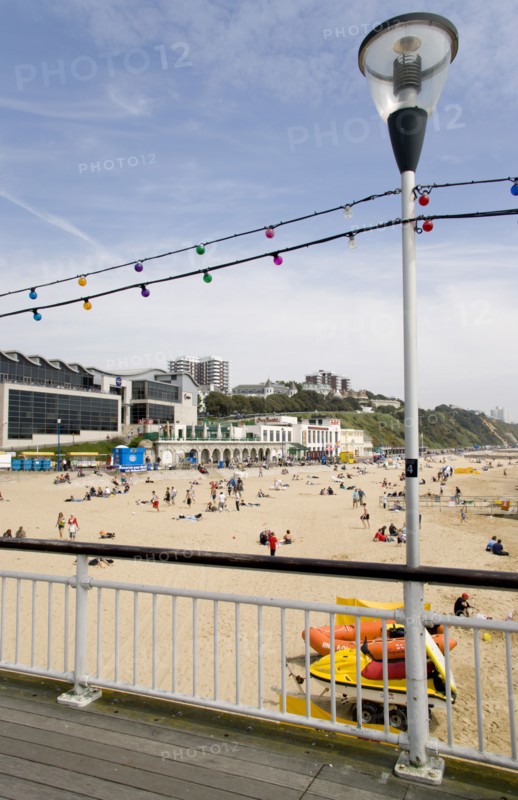 ENGLAND, Dorset, Bournemouth, The East Beach from the pier with seafront restaurants and bars. Adults and children play in the sand on the beach and at the water's edge. Hotels and flats line the clifftop into the distance