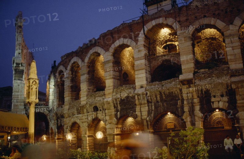 ITALY, Veneto, Verona, Teatro Romano.  Exterior facade of ruined theatre built in the 1st century BC illuminated at night with passers by in blur of movement in foreground.