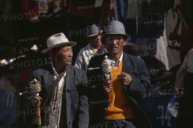 CHINA, Tibet, Lhasa, Pilgrims with prayer wheels walking through the Barkhor Bazaar
