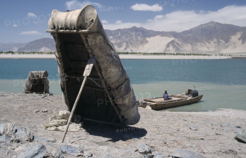 CHINA, Tibet, "Near Tsetang. Yak skin boats, one propped up by a paddle, and a local ferry beside the Yarlung Tsangpo, Brahmaputra River."