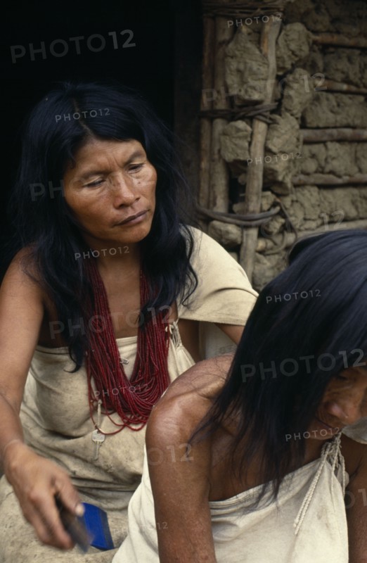 COLOMBIA, Sierra Nevada de Santa Marta, Sierra Avingue, Parque Nacional. Kogi mother and grandmother sit outside family home in Avingue  Mother combs head lice out of old grandma's hair. She wears many strands of dark red glass beads  the favourite colour of Kogi women and a sign of great wealth