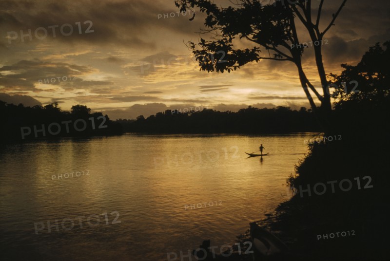 COLOMBIA, Choco Region, Noanama Tribe, Boy paddling canoe on lower rio San Juan at sunset