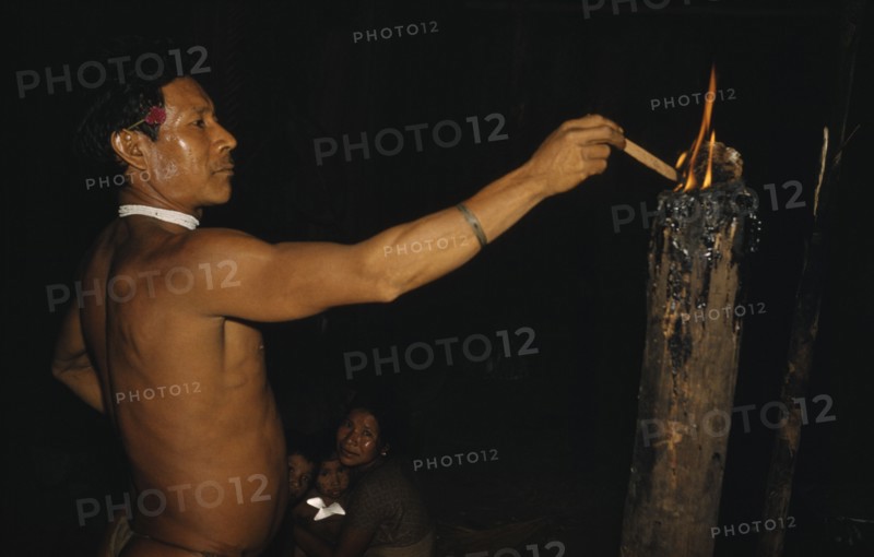 COLOMBIA, Vaupes Region, Tukano Tribe, Headman lights a “breo” resinous torch in centre of the “maloca” / longhouse.