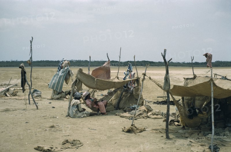 COLOMBIA, Guajira Peninsula, Guajiro / Wayuu Tribe, Portete a coastal desert settlement.  Wayuu encampment consisting of shelters of hardwood poles and old sacks. Women sewing inside central shelter.
