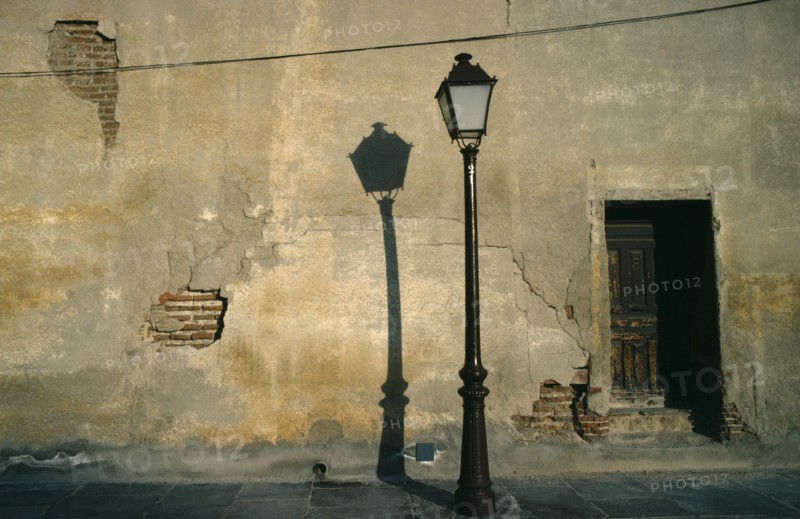 SPAIN, Madrid, Street lamp casting shadow against cracked and peeling plaster wall.