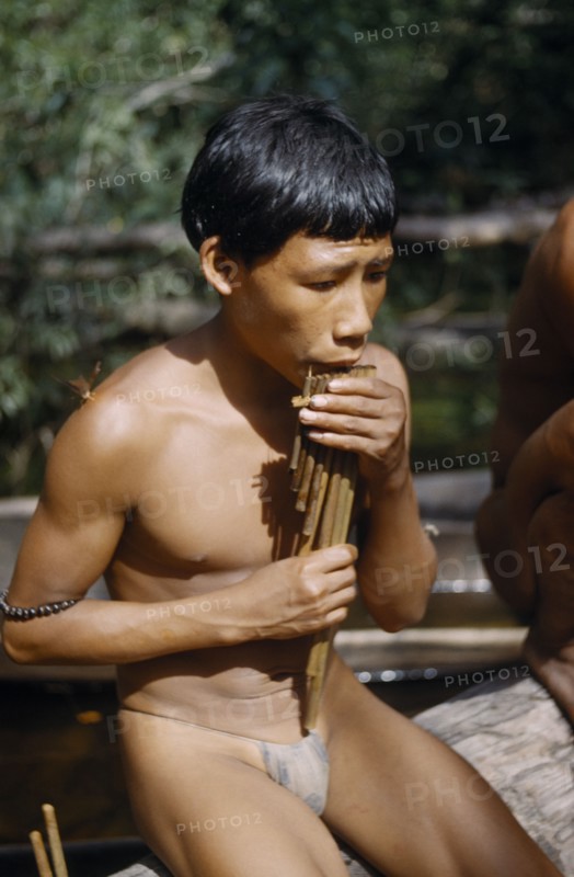 COLOMBIA, Vaupes Region, Tukano Tribe, Boy playing the “carizu” / panpipes at the maloca’s river port on the rio Piraparana