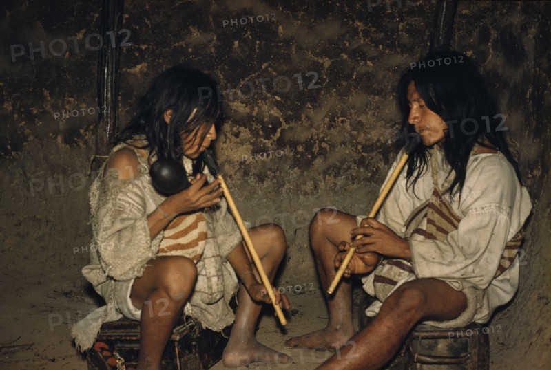 COLOMBIA, Sierra Nevada de Santa Marta, Kogi Tribe, Men playing “kuisi” flutes in San Miguel village. “macho” male flute has one hole and player waves a maraca; “embra” female flute which has five holes and maintains the melody.