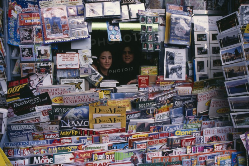 ITALY, Campania, Naples, Two women looking out from newsagents stall completely surrounded by newspapers and magazines.