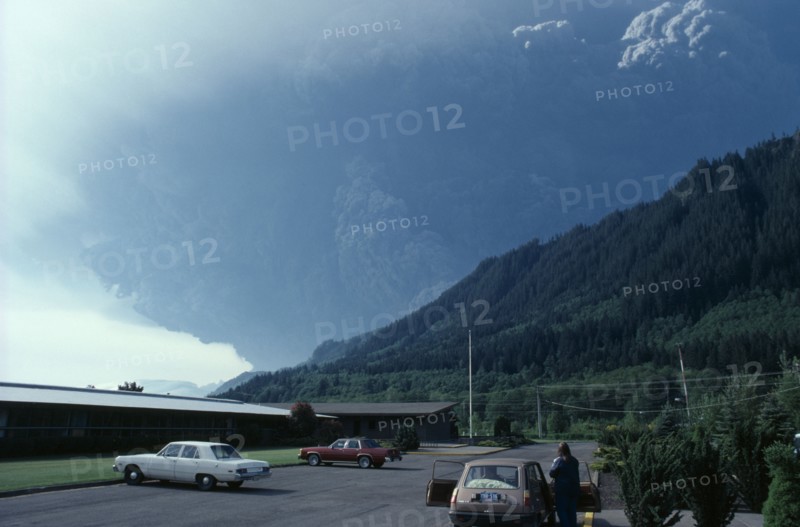 USA, Washington State, Mount St Helens Volcanic eruption 1980 at 8.40am. View from car park with a person standing outside a car looking towards forest covered mountain with billowing ash rising