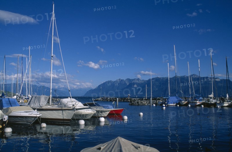 SWITZERLAND, Vaud, Lutry, Boats moored in marina with view across Lake Geneva beyond.