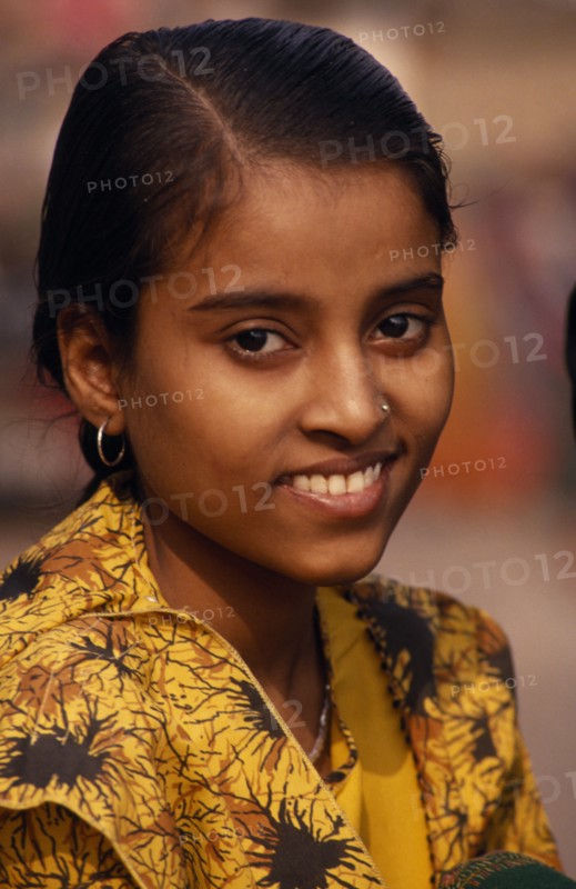 INDIA, Uttar Pradesh, Varanasi, Head and shoulders portrait of young girl on the ghats wearing a yellow shirt with a nose stud and earrings.