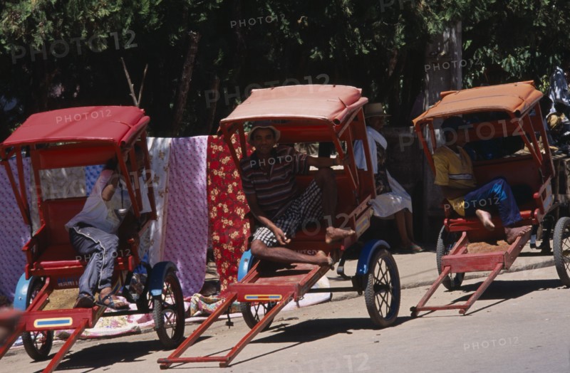 MADAGASCAR, Ambositra, Men drivers sitting in the shade of their Rickshaws waiting for a fare