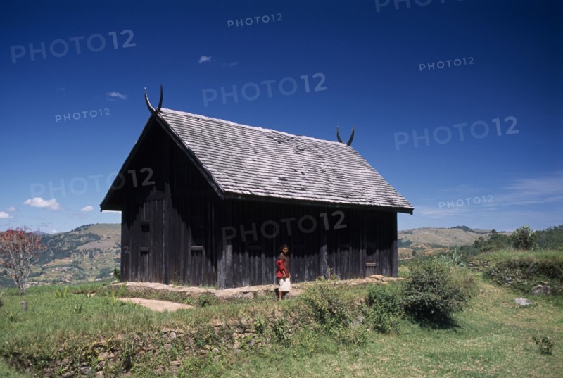 MADAGASCAR, Architecture, Near Ambositra. Royal wooden hut used by former Malagasy King with a woman standing outside exterior