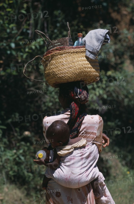 MADAGASCAR, People, Women, Near Ambositra. Portrait of a woman carrying a baby in a sling on her back and wicker baskets on her head