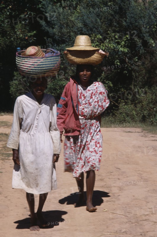 MADAGASCAR, People, Women, Near Ambositra. Two barefooted women walking up a dirt track carrying wicker baskets on their heads