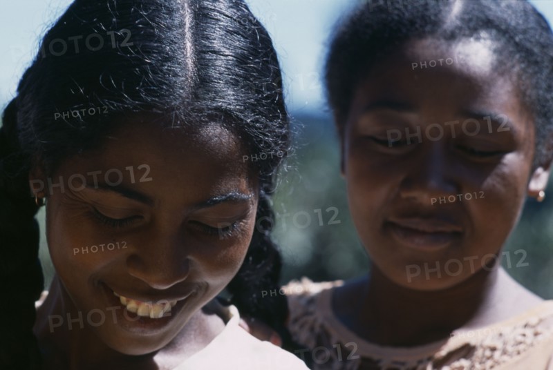 MADAGASCAR, People, Women, Road to Ranomanfana. Portrait of two young women smiling with their eyes looking down one girl with plaited pig tails