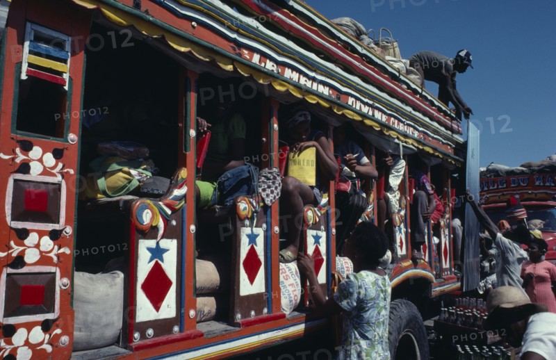HAITI, Transport, Colourfully painted bus with people loading goods onto the roof