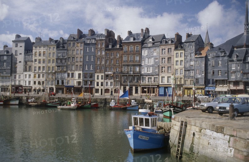 FRANCE, Normandy, Calvados, "Honfleur harbour with fishing boats moored against stone quay overlooked by tall, narrow houses."