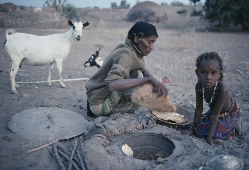 ETHIOPIA, North East, Afar tribeswoman baking bread in ground with child sitting beside her.