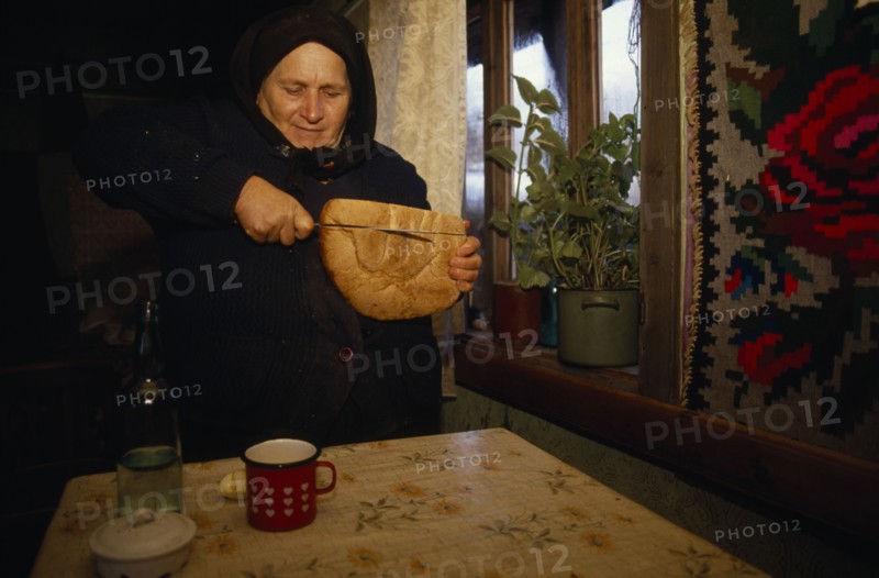 ROMANIA, Maramuresh, Elderly widow cutting bread.